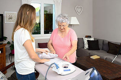 Betreuerin hilft älterer Dame beim Bügeln der Wäsche